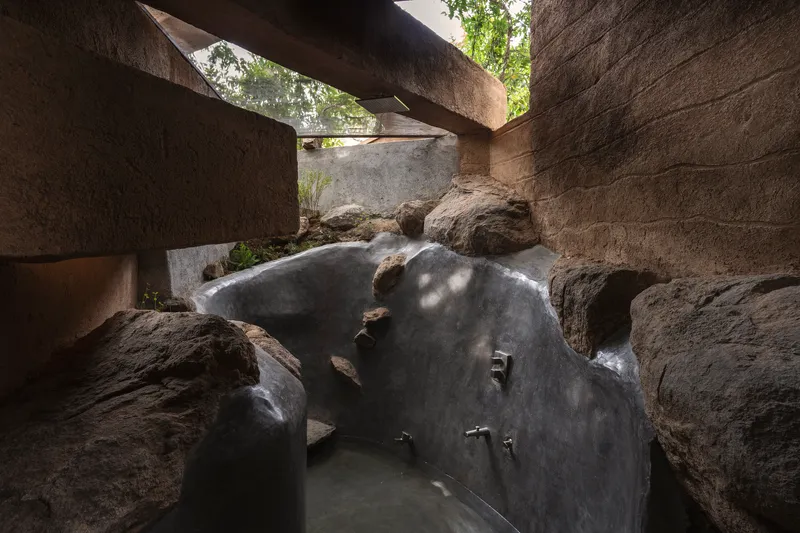 Sunken bathing pool carved into natural rock beneath concrete cantilevers and dappled light