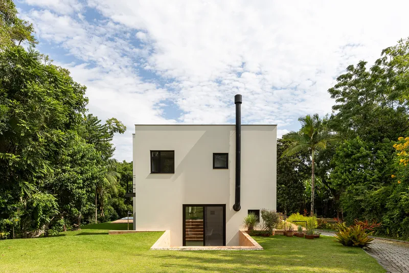 Rear facade with external black chimney pipe and square window openings framed by lawn and palms