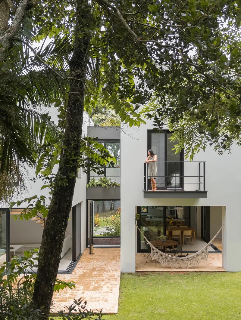 Cantilevered balcony with steel railing and figure seen through trees next to glazed living space