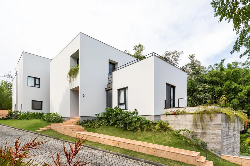 Street view of white stucco volumes on terraced lawn with timber-edged steps and concrete retaining wall
