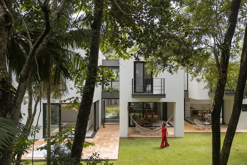Garden courtyard view with person in red dress walking across lawn between white volumes and mature trees