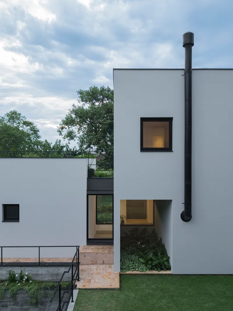 External black metal chimney flue rising along the white facade above recessed glazed entry