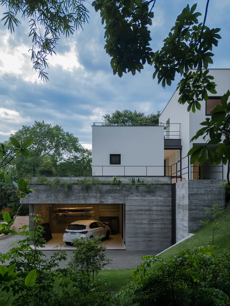 Board-formed concrete garage base with open door revealing parked car beneath white upper volume