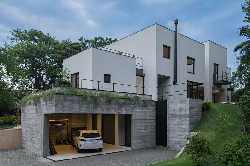 Front view of the concrete podium garage with white plastered volumes and metal railings above