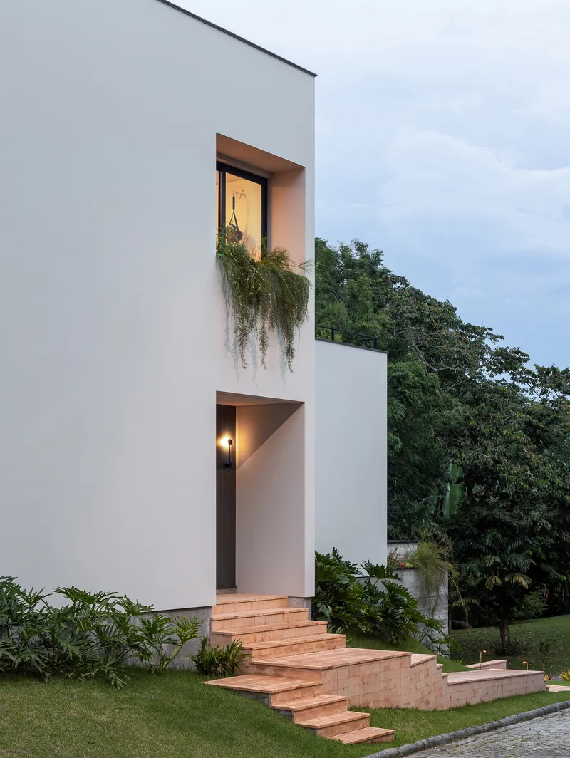 White facade with recessed openings and timber steps ascending through the lawn at dusk