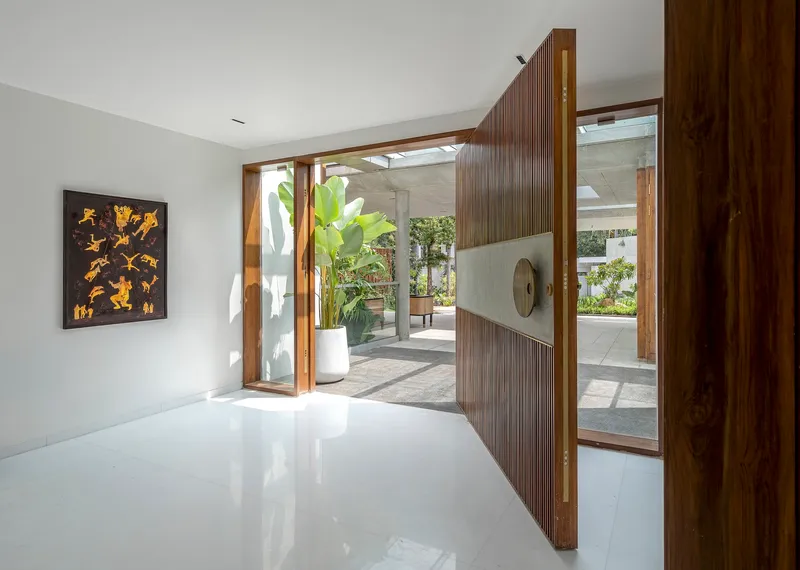 Entry foyer with pivoting timber door opening to concrete columns and greenery beyond