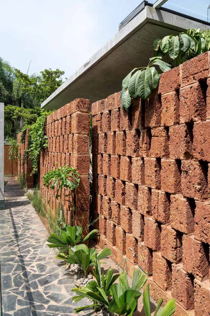 Perforated red volcanic block wall with concrete canopy above and tropical planting along the paved walkway