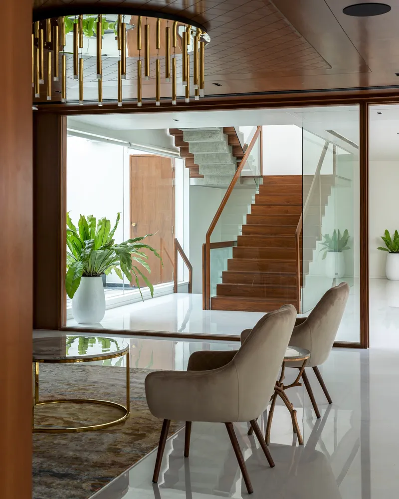Dining area with brass chandelier overlooking the timber and glass staircase through a wood-framed window