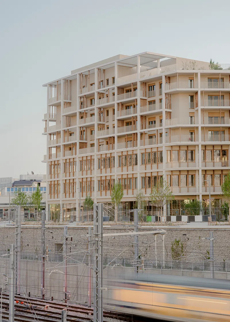 Exposed timber frame facade rising above railway tracks with young trees planted at ground level