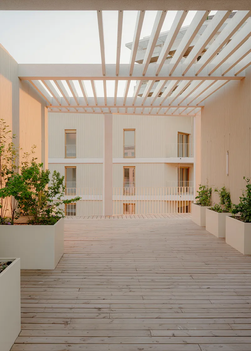 Rooftop terrace with timber decking and slatted pergola overhead framing views of the courtyard facade