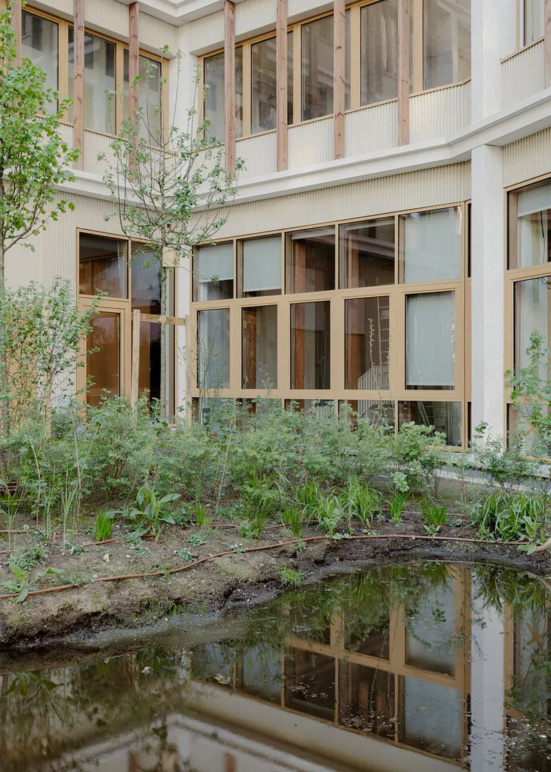 Internal courtyard with planted beds and shallow reflecting pool mirroring the timber-framed facade