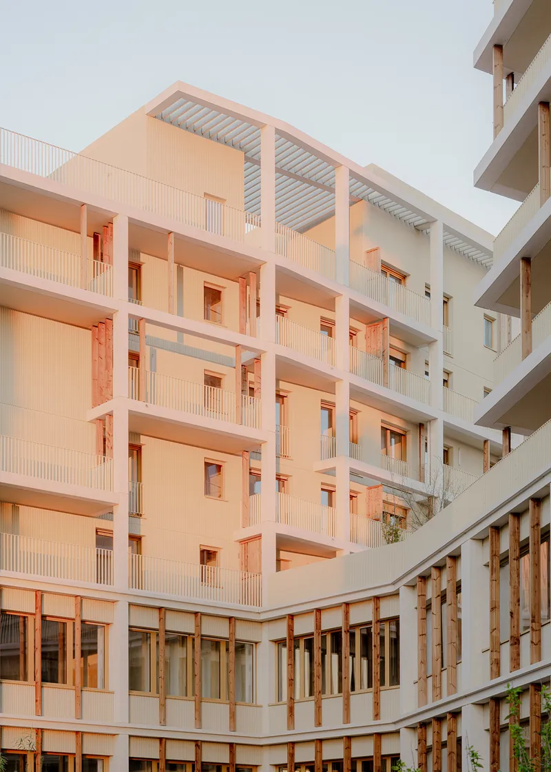 Multi-story courtyard elevation with white balconies and timber-framed openings in warm evening light