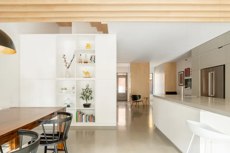 Open plan living space with exposed timber joists spanning above white shelving and kitchen island