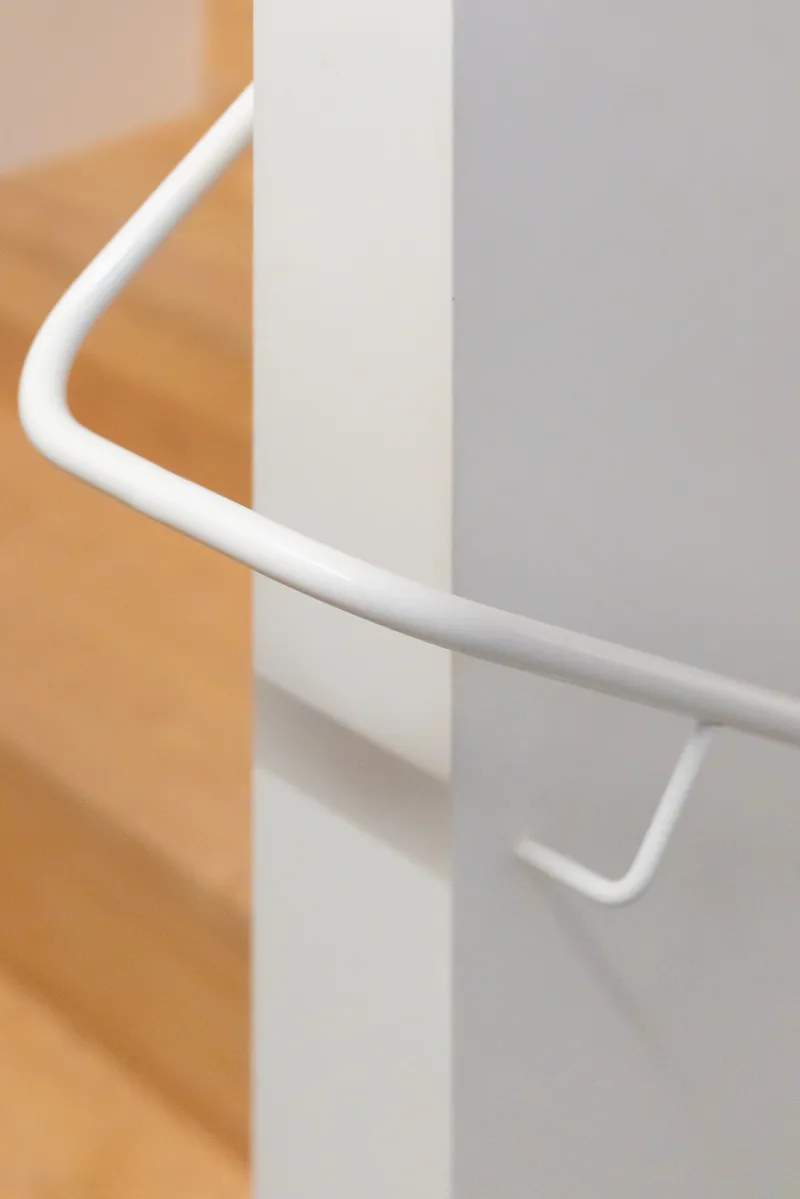 Detail of a white tubular metal handrail mounted on a white wall beside yellow tiled surfaces