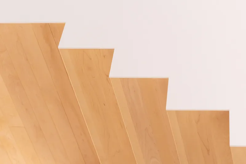 Side view of blonde timber stair treads stepping up diagonally against a white wall