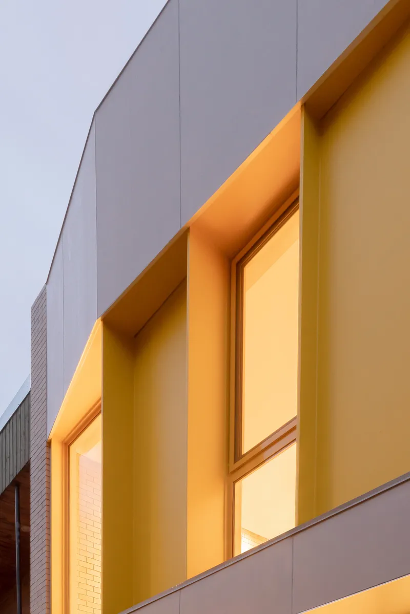 Close-up of the recessed yellow window frames against grey panel cladding at twilight