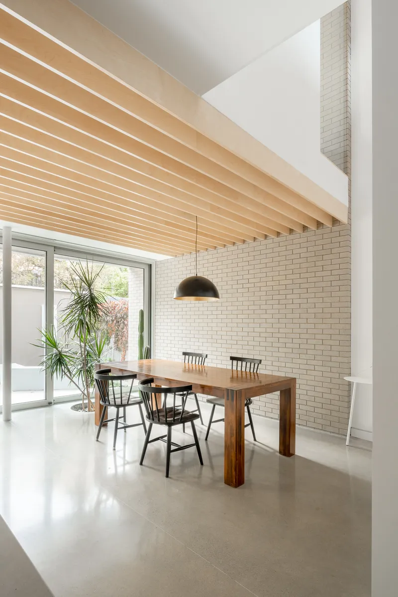 Dining area with white brick wall, exposed timber ceiling joists, and glazed doors to garden