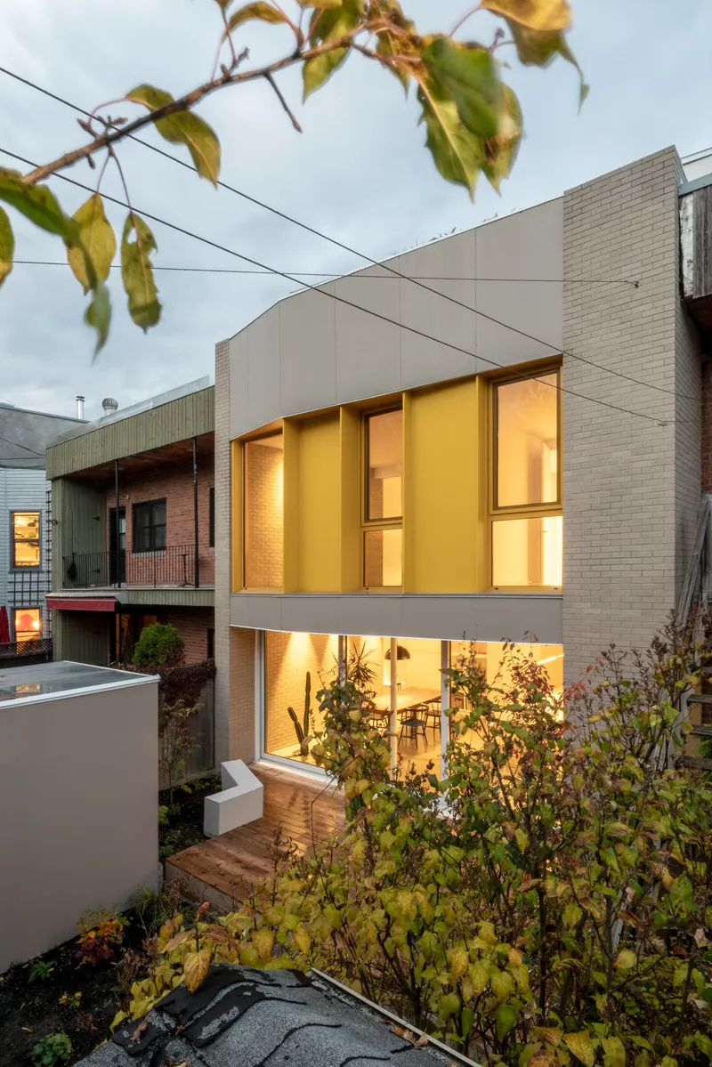 Street view of the multi-level rear facade with yellow window frames framed by autumn foliage