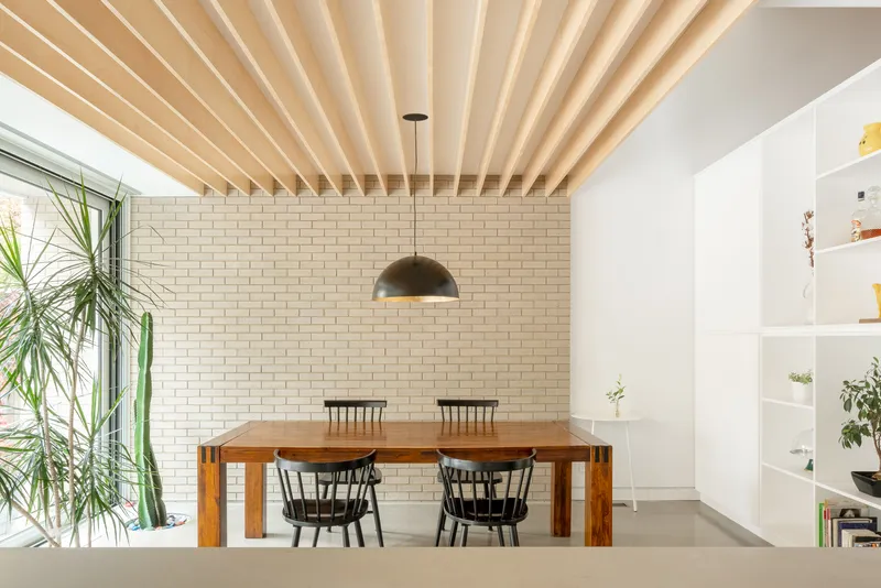 Dining room with exposed timber beam ceiling and cream brick wall beside a window with plants