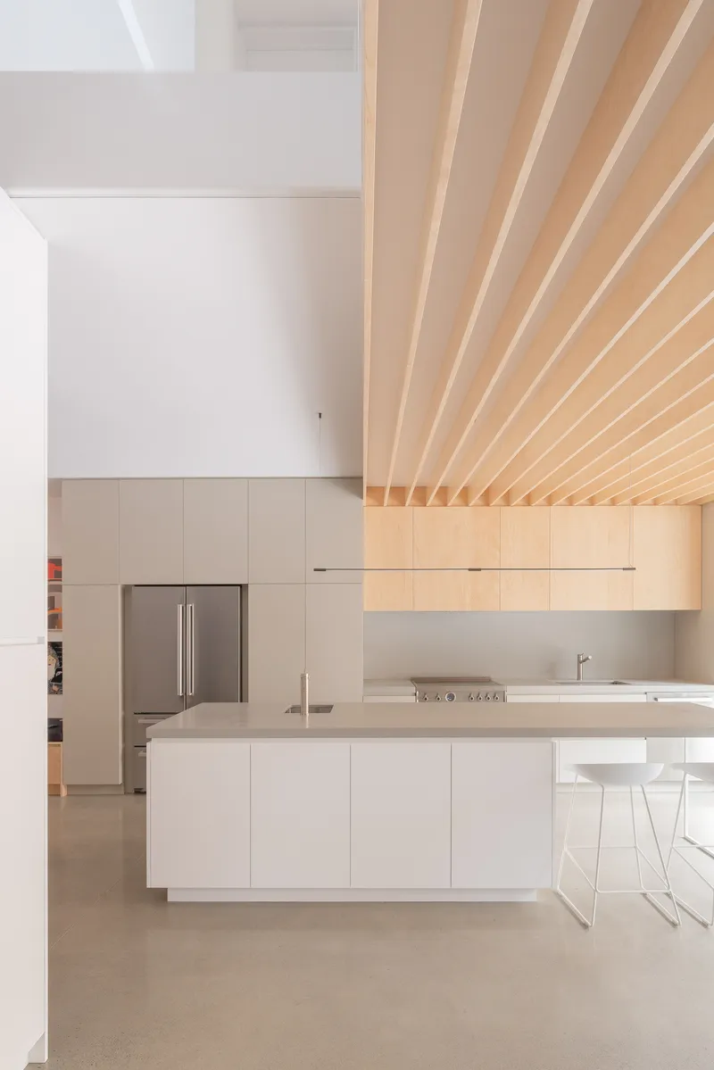 Kitchen with white island and ribbed timber ceiling transitioning into white painted volume
