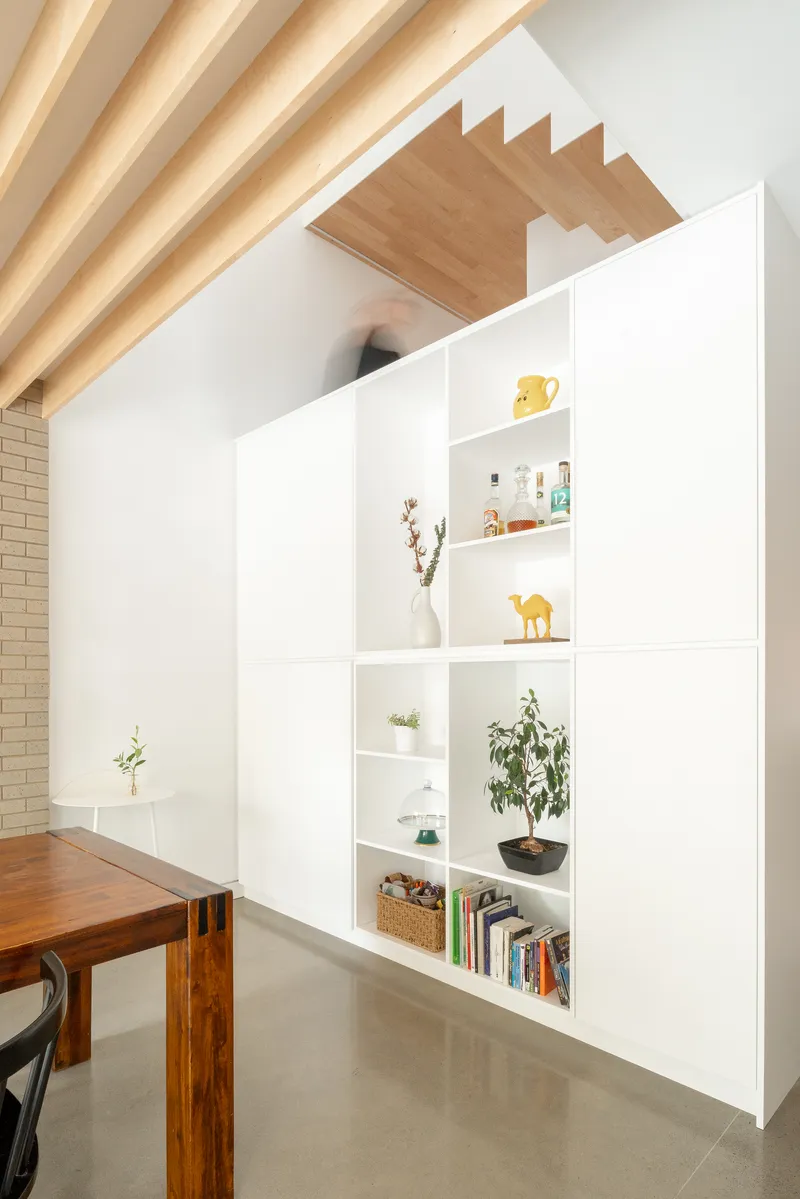 White shelving unit beside wooden dining table with view of timber stair soffit above
