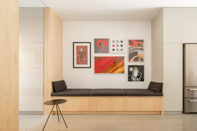 Built-in bench with cushions beneath a gallery wall of framed prints in red tones