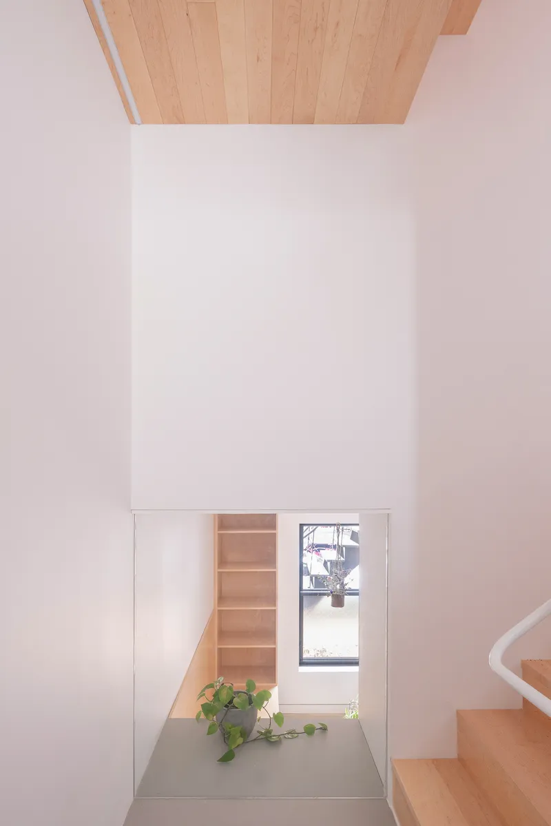 Double-height interior space with timber ceiling above white walls and a sunken alcove with shelving and a potted plant