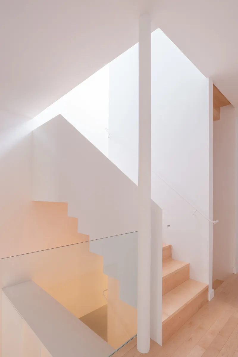 Light timber staircase wrapping around a white column beneath a triangular skylight