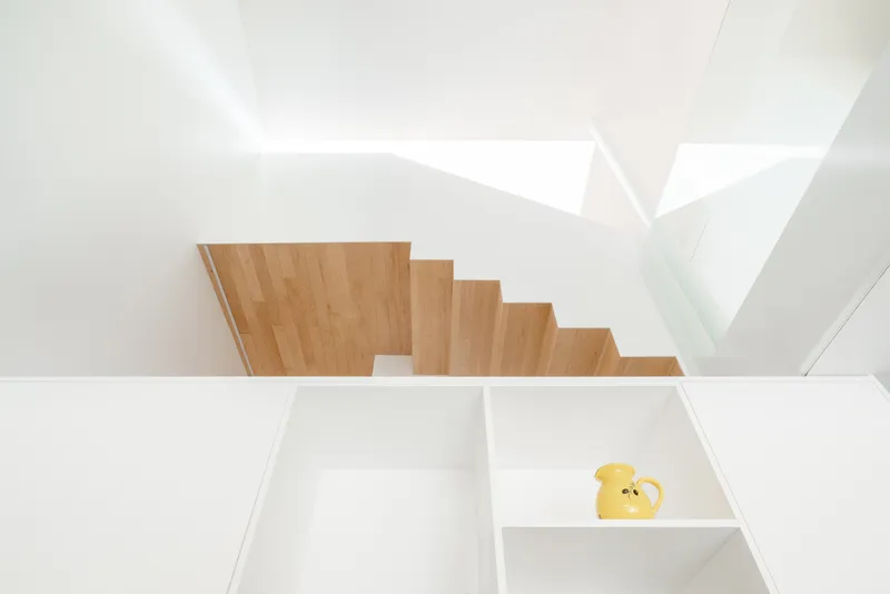 Overhead view of light timber stairs descending past white storage compartments with a yellow pitcher inside