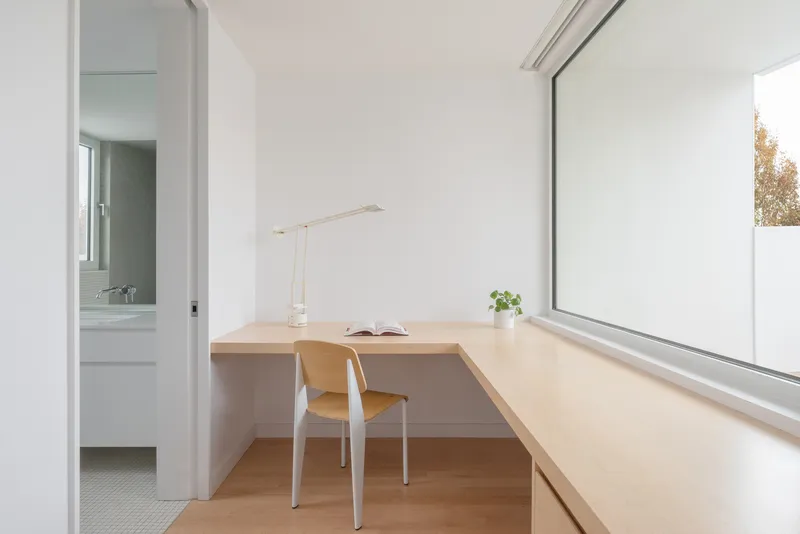 Built-in timber desk with a chair beneath a large window framing autumn trees outside