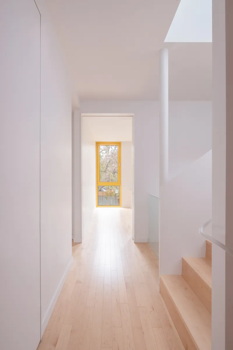 Narrow hallway with light timber flooring leading to a yellow-framed window at the end
