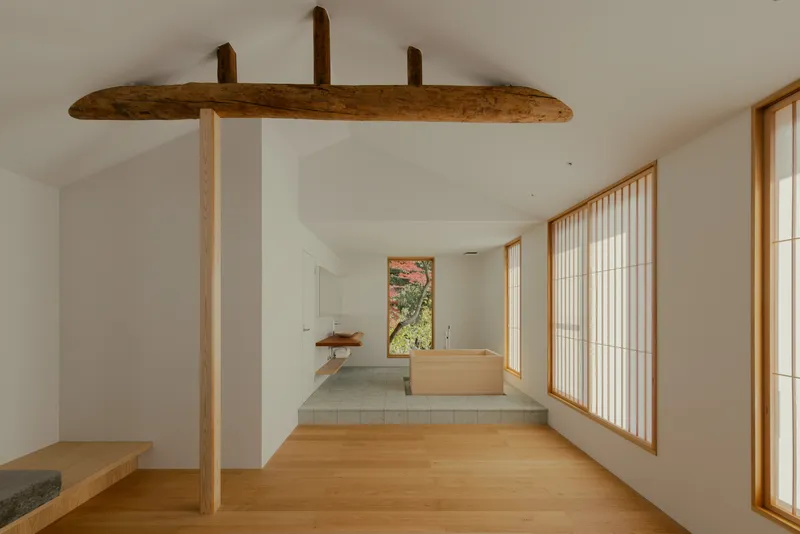 Interior view showing reclaimed timber beam above a step-up tea room with shoji screens and autumn foliage beyond
