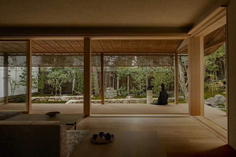 Timber-framed pavilion opening onto a rock garden with moss, stones, and a seated Buddha sculpture
