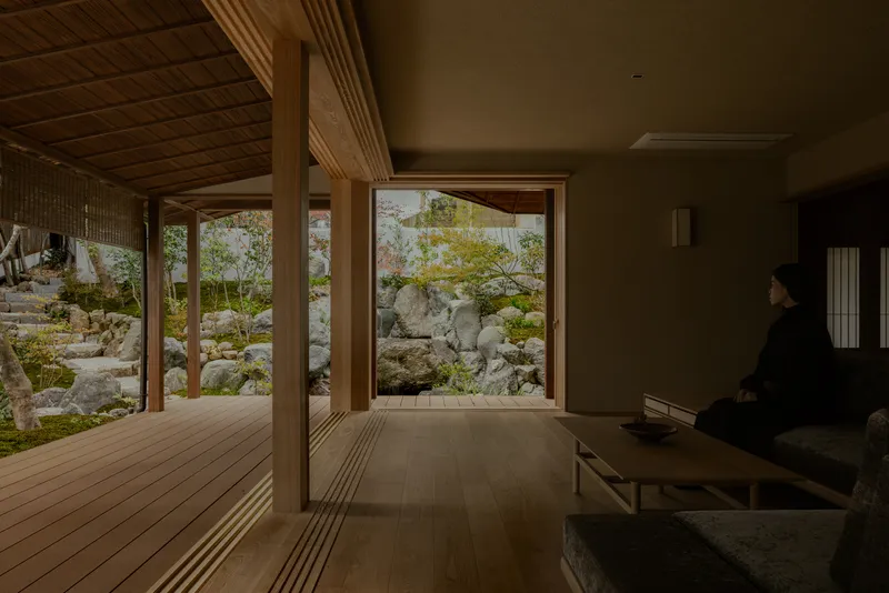 Seated figure beside a picture window framing a moss garden with large boulders and small trees