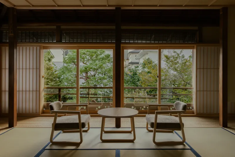 Tatami room with low wooden chairs and table overlooking trees through sliding shoji screens