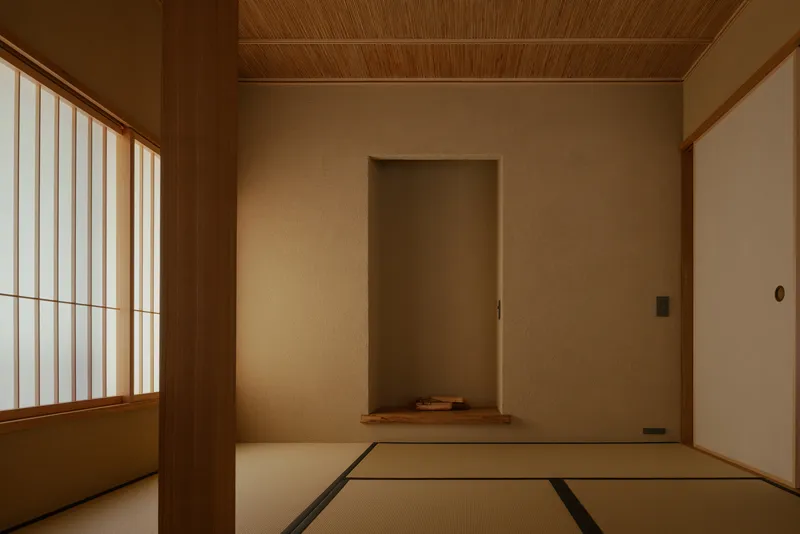 Tatami room with shoji screen, recessed alcove, and timber-lined ceiling in warm light