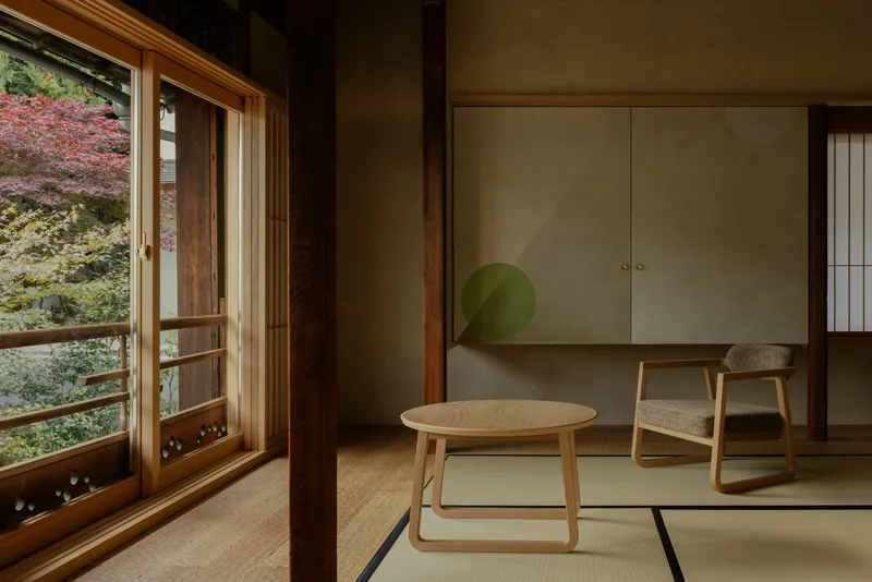 Tatami room with low table, chair, and sliding doors opening to autumn foliage