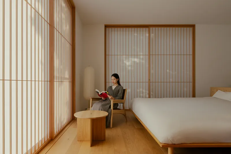 Bedroom interior with timber-framed translucent sliding screens and a woman reading beside the bed