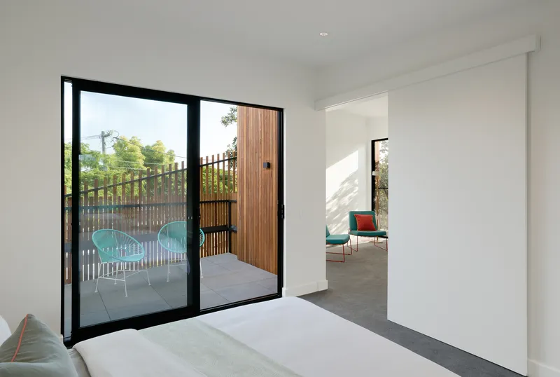 Bedroom with black-framed glass doors opening to a terrace with timber screening and turquoise chairs