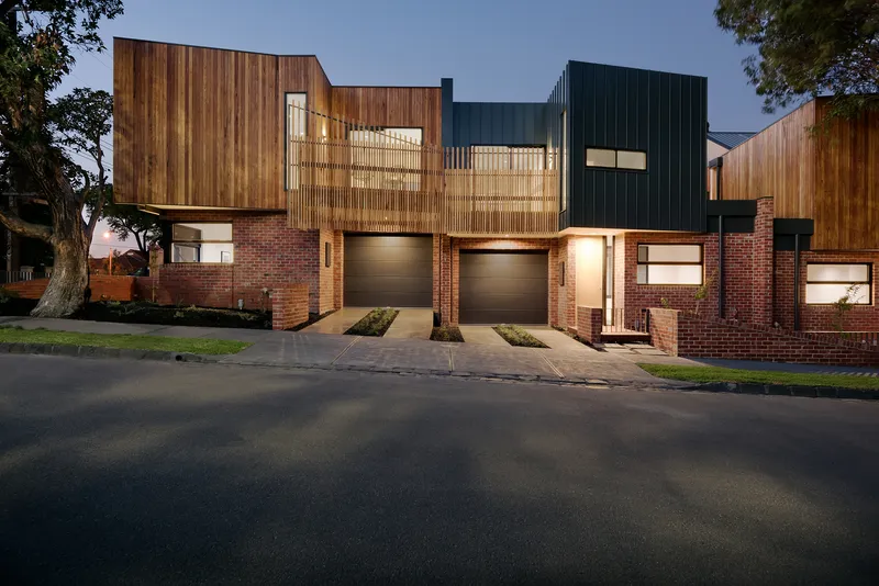 Front facades with vertical timber screens, brick bases, and illuminated garages beneath eucalyptus trees at dusk