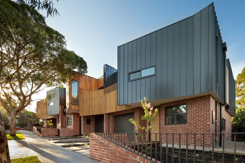 Street view of row housing with red brick base, timber cladding and charcoal metal volumes in afternoon light
