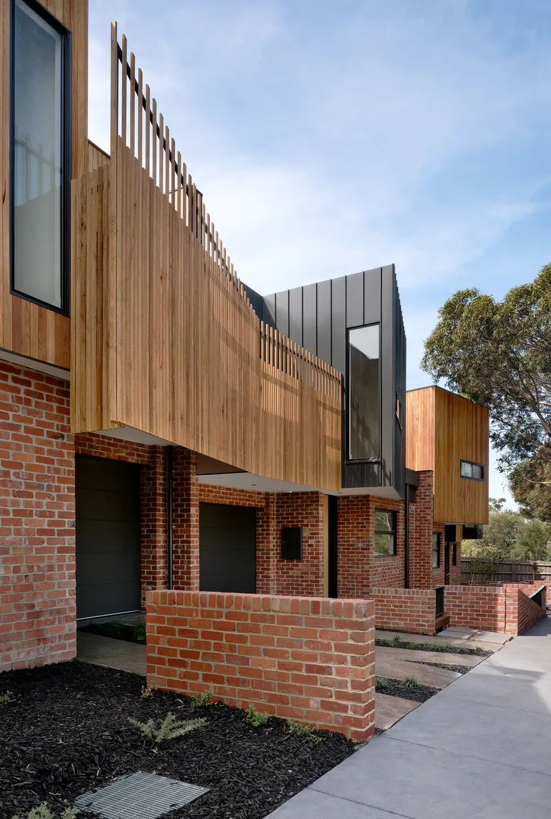 Entry sequence with red brick wall, vertical timber screen and planted bed along concrete path