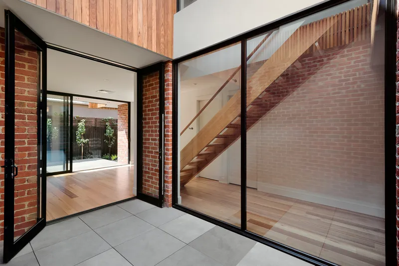Entry threshold with glass doors opening to timber stair beyond exposed brick wall