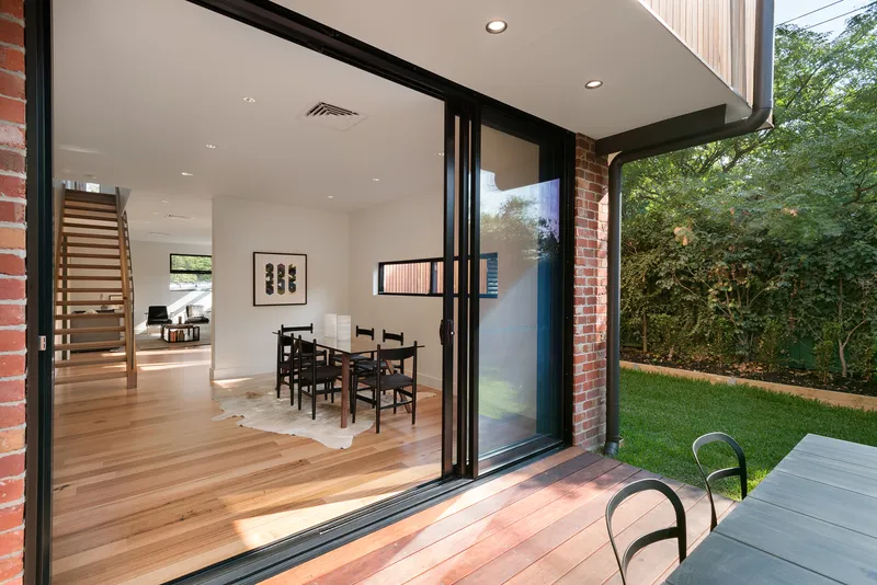 Open sliding glass doors connecting dining room with timber floor to rear lawn