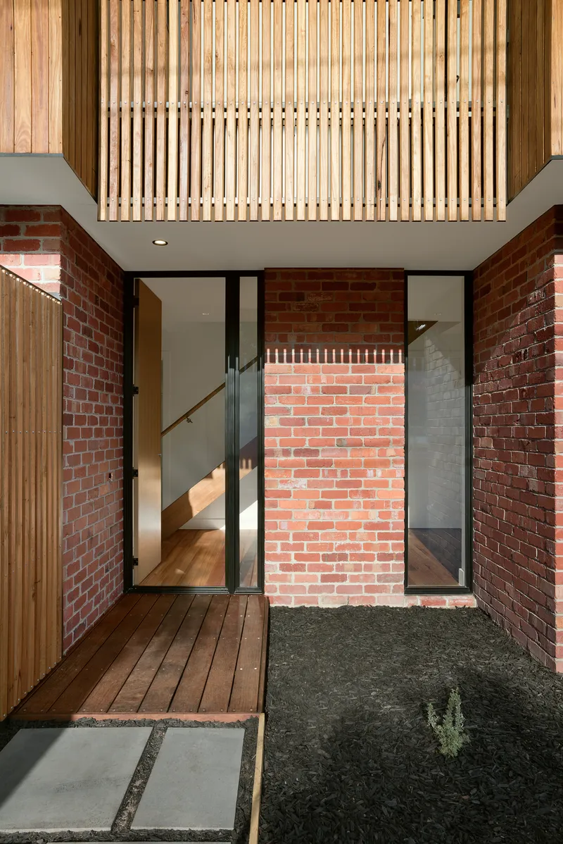 Courtyard view showing timber slatted screen overhead and brick walls flanking glazed entry doors