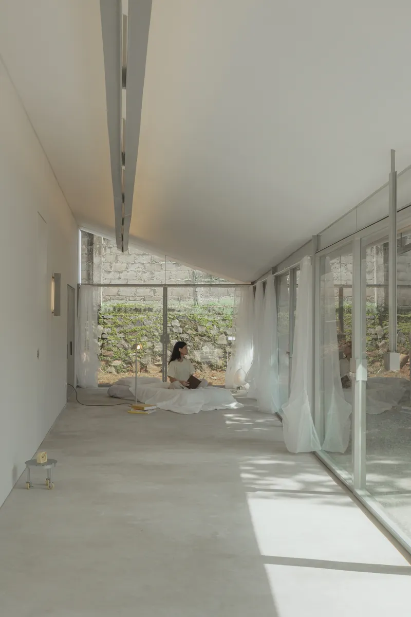 Interior hallway with full-height glazing overlooking a planted courtyard with a seated occupant inside