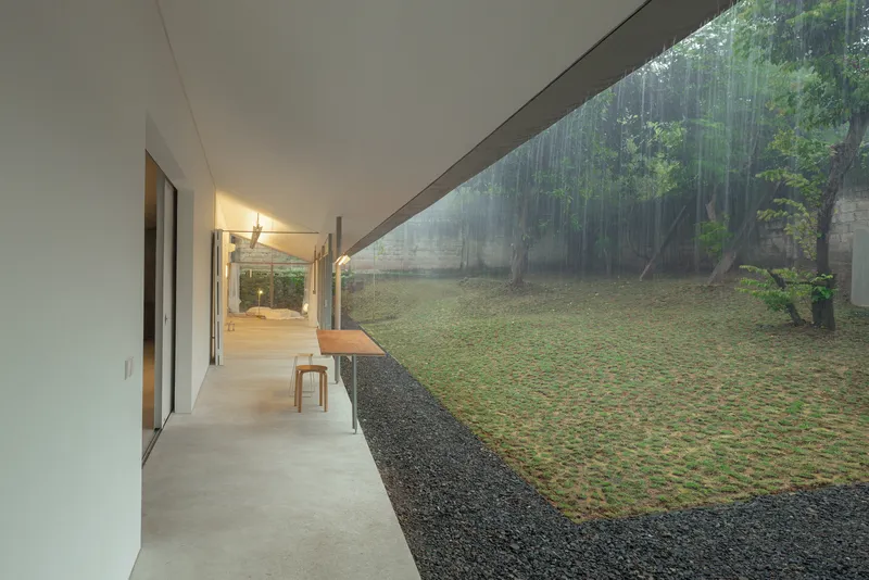 Covered exterior corridor with concrete floor looking toward the garden through columns of rain