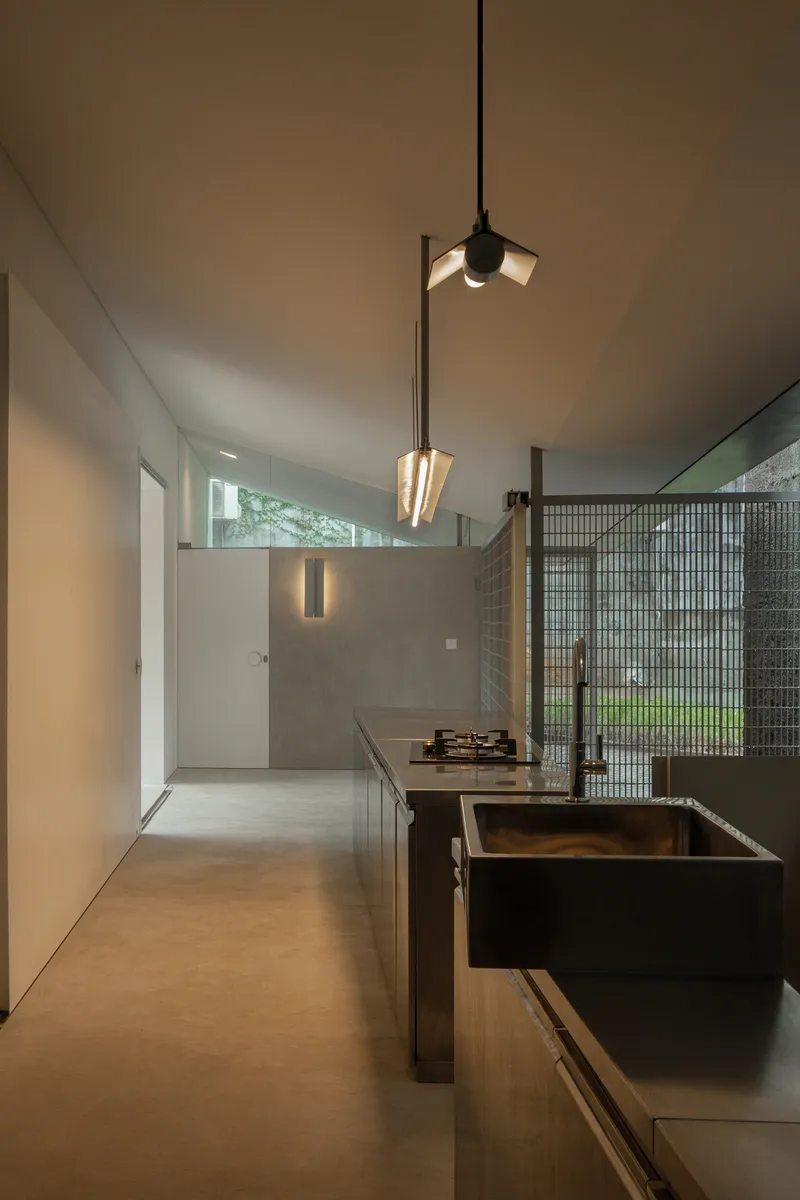 Kitchen island with dark steel sink and pendant lights suspended from the angled ceiling