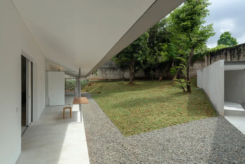 Covered terrace overlooking gravel and grass courtyard with existing trees and weathered concrete walls