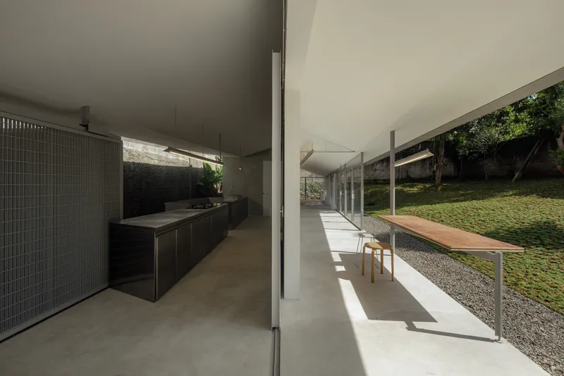 Open kitchen with black cabinetry and long dining table extending toward the sunlit garden courtyard